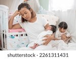 Small photo of tired mother suffering from experiencing postnatal depression sitting on bed near children's cot. mother sleeping embracing to her asleep baby daughter sitting at home. single mom motherhood stressful
