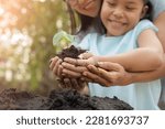 Small photo of hands holding young plant with soil.World environment day and sustainable environment concept. Mom and her child girl plant sapling tree. Teamwork protecting and reduce global warming earth.