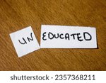 Small photo of Torn, white paper sheet with inscription uneducated on brown wooden office desk. Uneducated status is over. Education concept, parhayi likhayi, education, educated, importance of education. Positivity