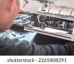Small photo of Male master repairs the sewing machine. Inspection of the mechanism in search of a breakdown. Professional adjustment of a sewing machine. Cleaning and repair of professional equipment.