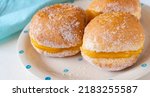 Small photo of Bola de Berlim, or Berlin Ball, a Portuguese pastry made from a fried doughnut filled with sweet eggy cream on the table