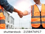 Small photo of Asian male civil engineer in safety vest shaking hands for agreement in housing estate project with subcontractor at construction site