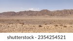 Small photo of vast desert landscape with rugged mountains, devoid of human presence, where the interplay of light and shadow highlights the austere beauty of nature's untouched expanse.