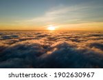 Aerial view of vibrant yellow sunrise over white dense clouds with blue sky overhead.