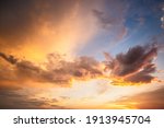 Dramatic sunset landscape with puffy clouds lit by orange setting sun and blue sky.