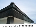 Small photo of House corner with brown metal planks siding and roof with steel gutter rain system. Roofing, construction, drainage pipes installation