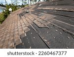 Small photo of Wind damaged house roof with missing asphalt shingles after hurricane Ian in Florida. Repair of home rooftop concept