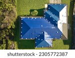 Small photo of Aerial view of damaged in hurricane Ian house roof covered with blue protective tarp against rain water leaking until replacement of asphalt shingles