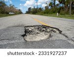 Small photo of Damaged american road surface with deep pothole. Ruined street in urgent need of repair