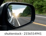 Inside view of mirrors wing. Rear view of a gray car with asphalt road and green trees in the daytime. Clear traffic in rural areas.