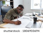 Afro-American architect working in office with blueprints.Engineer inspect architectural plan, sketching a construction project. Portrait of black handsome man sitting at workplace. Business concept.