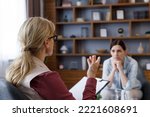 Over shoulder view of female psychologist sitting in armchair, talking with upset woman patient. Psychologist taking notes on clipboard. Psychology, mental therapy, mental health, therapy session