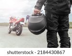 A man stands with his back to his motorcycle, holding a helmet