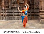 Indian classical Odissi dancer looks at the mirror during the Odissi dance recital against the backdrop of temple sculpture.art and culture of india. 