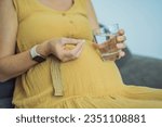 Prenatal Vitamins. Portrait Of Beautiful Smiling Pregnant Woman Holding Supplement and a glass of water, Taking Supplements For Healthy Pregnancy While Sitting On Couch At Home, Free Space