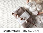 Small photo of Well groomed woman hand holding a cotton branch with stack of neatly folded linens near rolled up towels in mesh basket placed on knitted chunky merino wool yarn plaid. Natural textile. Top view.
