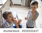 Small photo of Two funny little boys pick one's nose performing bad habit eating bread at kitchen medium shot. Cheerful male kids having fun with positive emotion fooling smiling enjoying happy childhood at home