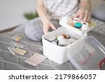 Closeup female hand neatly placing medicament at domestic first aid kit top view. Storage organization in transparent plastic box drug, pill, syringe, bandage. Fast health help safety emergency supply