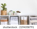 Small photo of Potted plants in ecology straw baskets on shelf of bed linens cupboard textile arrangement storage organization. Minimalism Scandi placed method neatly folded cotton fabric bedding material copy space