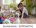 Small photo of Confident male kid building fortress tower architecture wooden bricks ecology Montessori material. Baby boy playing construction eco friendly rainbow bricks at nursery childish room home toys storage