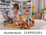 Small photo of Confident male kid building fortress tower architecture wooden bricks ecology Montessori material. Baby boy playing construction eco friendly rainbow bricks at nursery childish room home toys storage