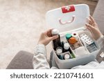 Small photo of Closeup female hand neatly placing medicament at domestic first aid kit top view. Storage organization in transparent plastic box drug, pill, syringe, bandage. Fast health help safety emergency supply