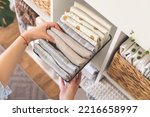 Small photo of Modern housewife putting neatly folded towels, pillowcases, duvet covers into plastic metallic case boxes use vertical method storage organization. Woman making seasonal tidying up at home cupboard