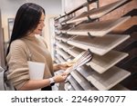 Happy brunette female interior designer choosing flooring tile color texture samples at store shop. Woman architect choice floor and wall finishing material for architecture and construction industry