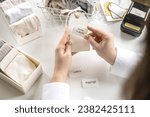 Small photo of Woman hands cutting sticker tag scissors comfortable storage organizing of linen textile in container. Female housekeeping sorting cotton clothes underwear with label tag mark organize domestic space