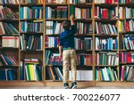 Back view, boy stretches after a book on multi colored bookshelf in library. Education, Knowledge, Bookstore, Lecture.