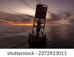 Small photo of Bell buoy floating on a calm ocean with a pastel sunset. Close up buoy photo