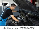 Small photo of Car mechanic noting repair parts during open car hood engine repair at garage. Mechanic man open a car hood and check up the engine. Overheating of a car engine. Motor with open hood.