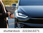 Unrecognizable elegant man using smartwatch app for remote controlling of premium class electric car, driver distantly approaching car and opening door, smart car.