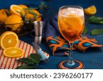 Small photo of aperol drink, with orange, leaves, blue masa, blue and orange cloth, red board with white dots, a dispenser and colorful holder