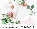 Office desk with notebook, rose flowers, eucalyptus branch, pink paper blank. Flat lay, top view, copy space.