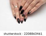 Black beige manicure with gold glitter and a gold stripe. Long sharp nails on a white background close-up.