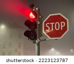 Red traffic lights glowing in the fog near big stop sign