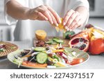Small photo of A woman makes a salad of fresh vegetables, squeezes the juice of a lemon, close-up, the concept of diet and healthy eating.