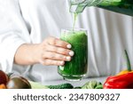 A woman pouring green smoothie to glass, healthy food concept.