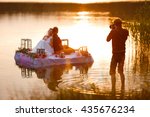 Wedding photographer in action, taking a picture of the bride and groom sitting on the raft. Summer, sunset