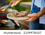 Man put down on a wooden board ready to eat grilled steak meat, male roasted steak meat on the gas grill on barbecue grill outdoor in the backyard, summer family picnic, food on the nature.
