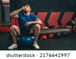 An Athelete is taking a break after a tough session workout. He is wearing a blue shirt and sitting on a blue ball