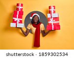 Christmas shopping African American woman holding many gifts in her arms wearing santa hat and red scarf in a round circle hole in orange background.