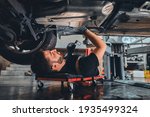 Male car mechanic worker working using wrench tool for repair, maintenance underneath car. Mechanic vehicle service checking under car in garage. Auto car repair service, maintenance concept.