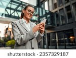 Successful attractive beautiful confident young business woman in glasses and jacket holding phone and looking at it. Corporate call before the meeting, communication and modern applications.