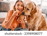 Small photo of Golden retriever eagerly licking paper box with chinese noodles being eating by young woman. Female pet owner sharing food with lovely furry friend at cozy apartment.