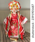 Small photo of Traditional Ukrainian doll Motanka. Motanka is red, she is decorated with traditional embroidery, on her head she has a big wreath with ribbons, the wreath is made of artificial flowers, roses.