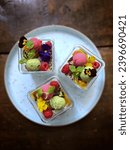 Small photo of Summer dessert of raspberry sorbet matcha sorbet edible flowers and berries in a glass jar served on a blue plate