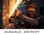 Small photo of Man with a grinder is building a fence from wood and concrete at outdoor. Bright sparks are flying from cutting metal abrasive disk of the angle grinder.
