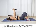 Small photo of Full body side view of fit young female lying on mat with heave weight plate in raised hands while training muscles during fitness workout at home